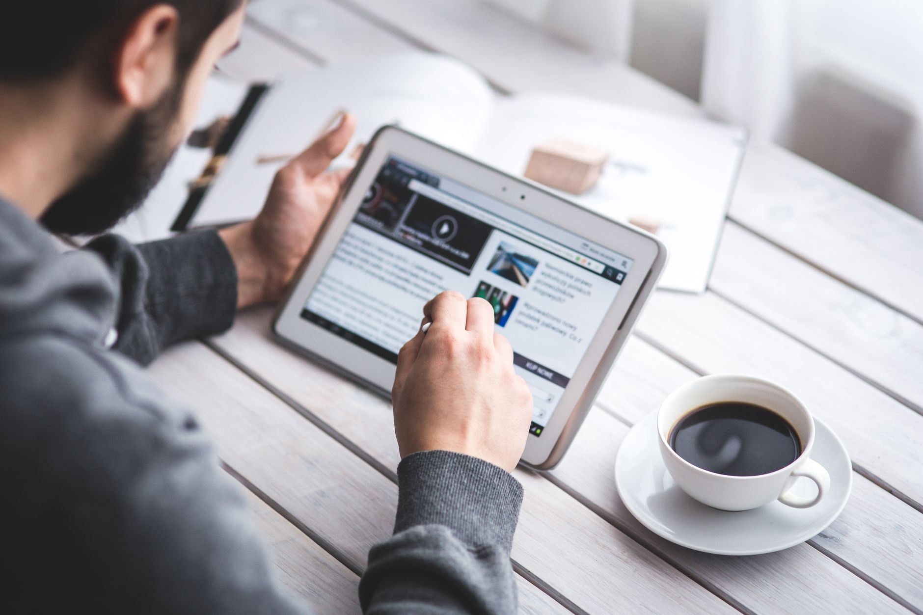 A man uses a tablet to browse news while enjoying a cup of coffee